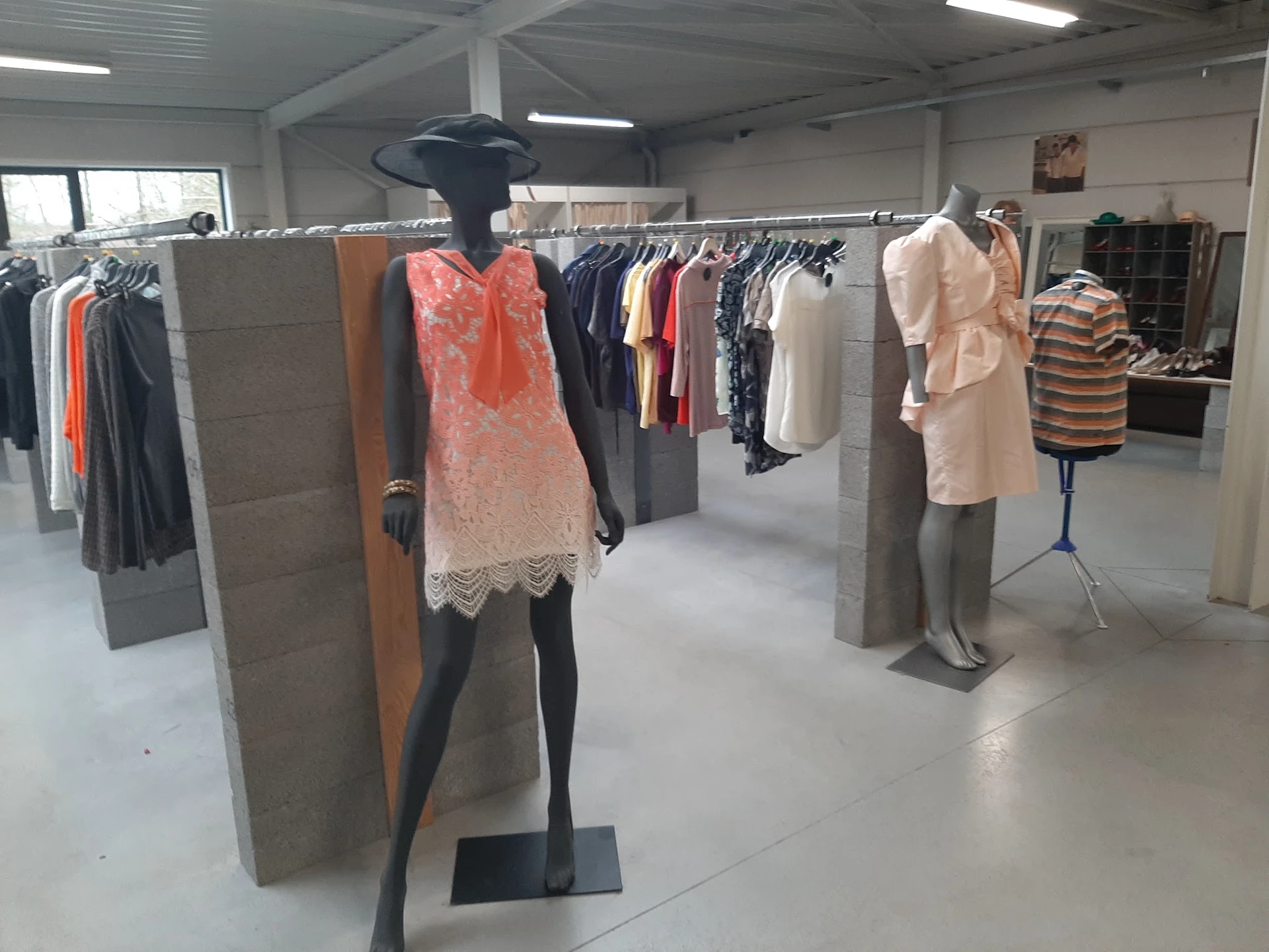 Kledingrekken met tweedehands dames- en herenkleding op etalagepoppen in een kringloopwinkel