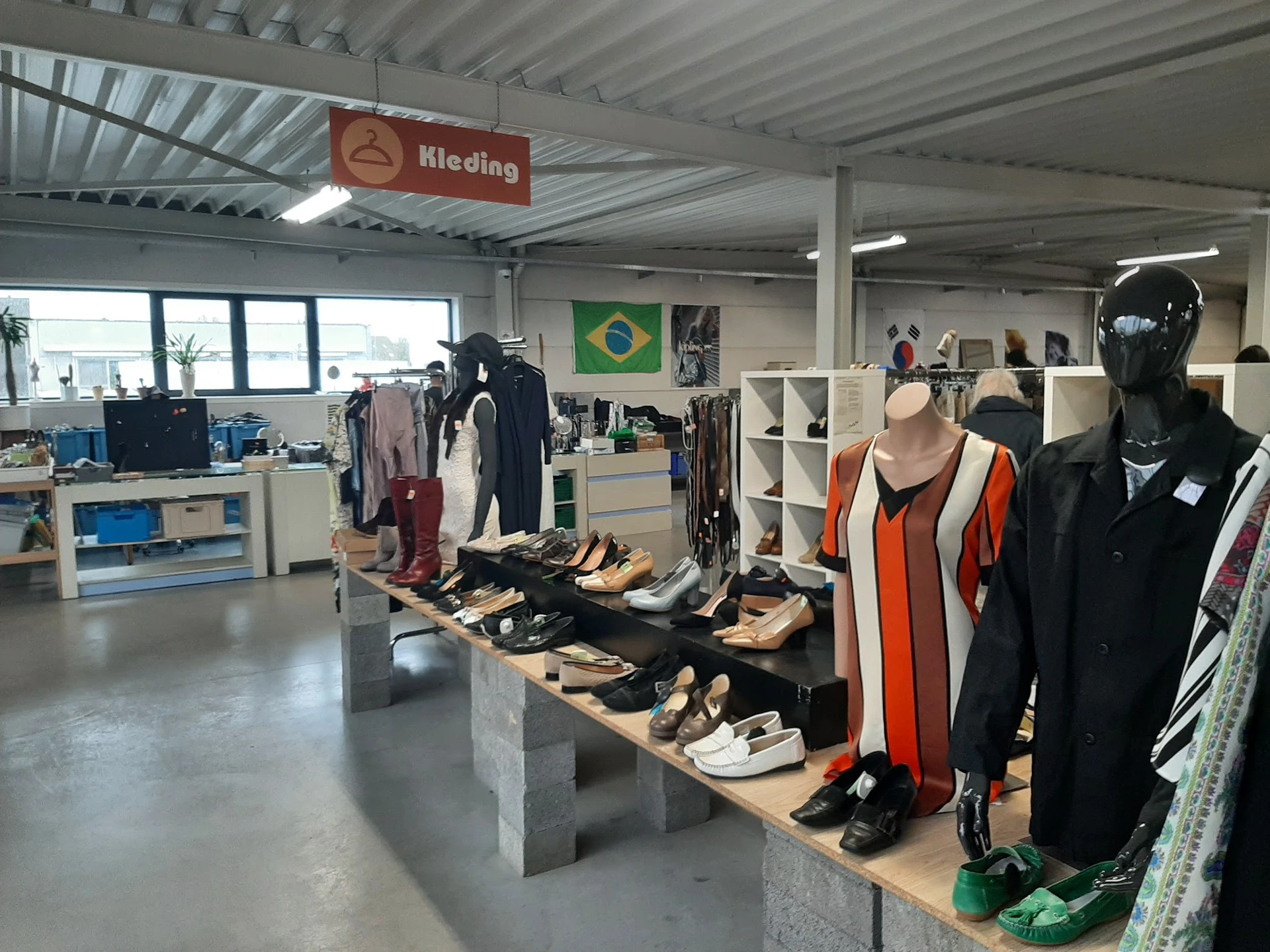 Uitgestalde tweedehands kleding en schoenen op tafels in een kringloopwinkel