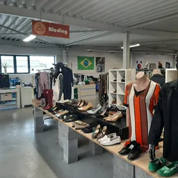 Uitgestalde tweedehands kleding en schoenen op tafels in een kringloopwinkel