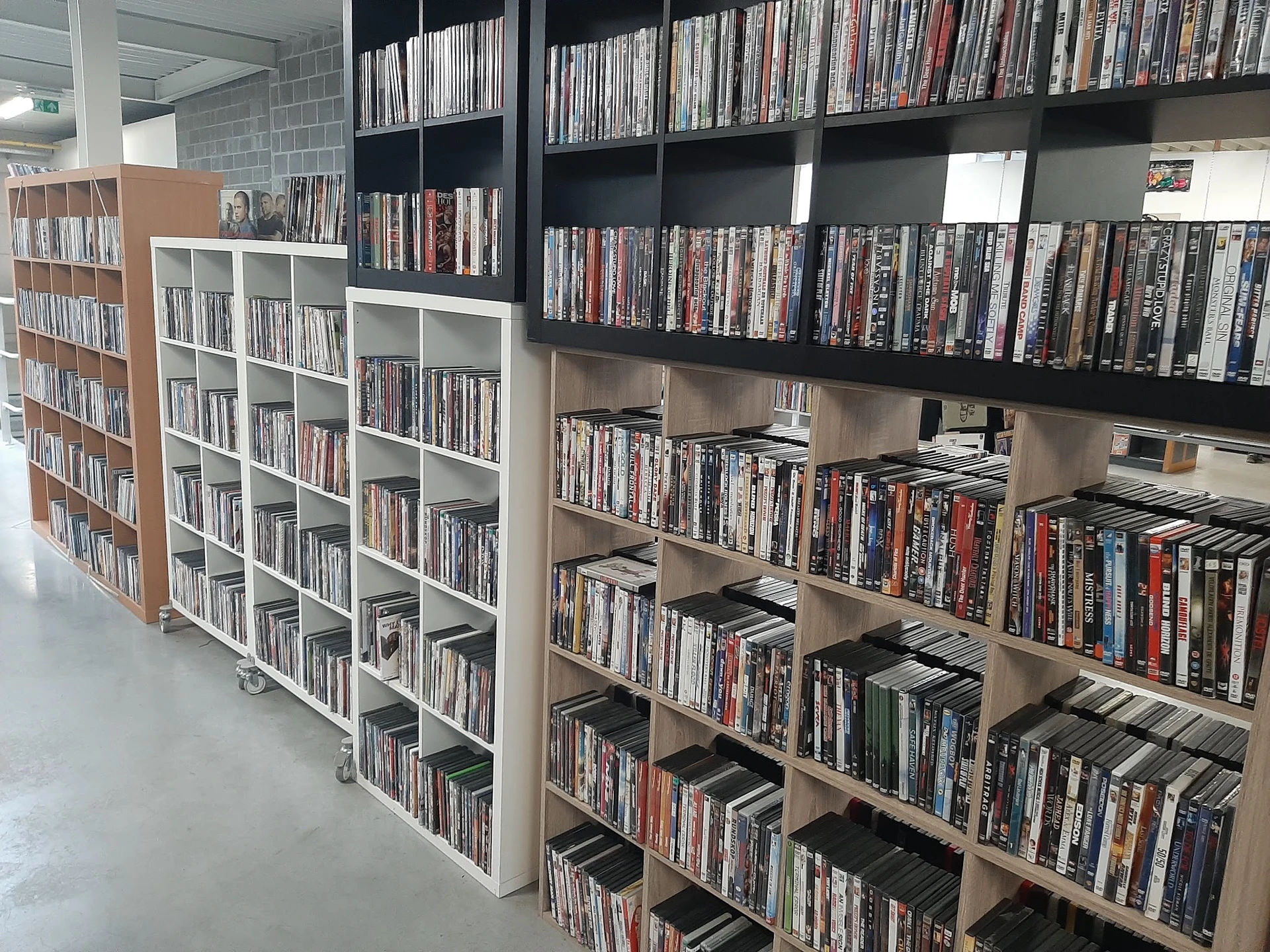 Uitgestalde dvd- en blu-ray-collecties op houten en witte stellingen in een kringloopwinkel