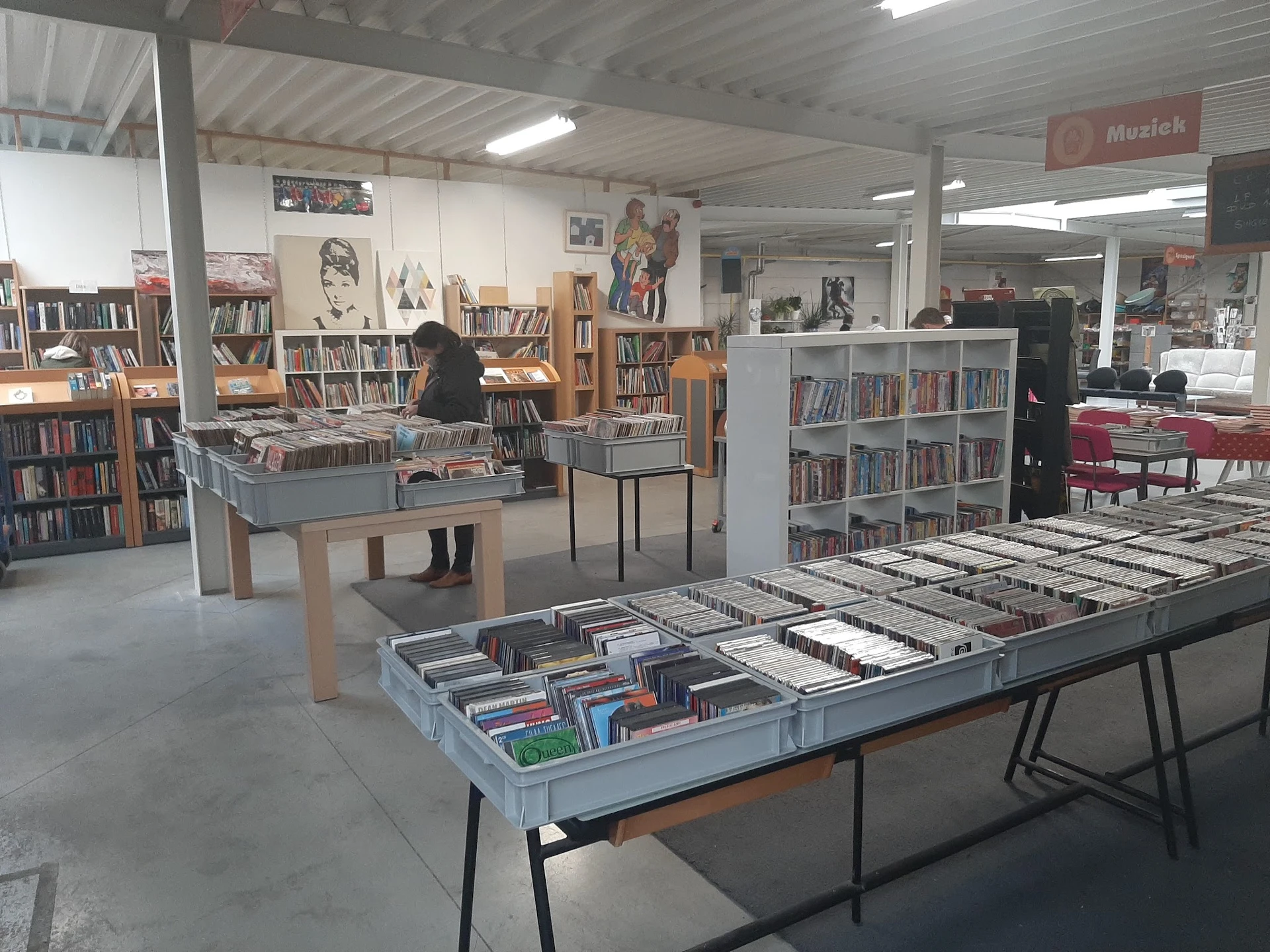 Winkelvloer met tafels vol cd's en dvd's, boekenkasten en muziekalbums in kringloopwinkel