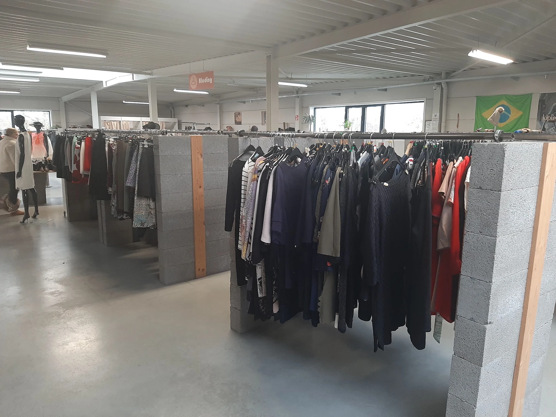 Rekken met tweedehands kleding in verschillende kleuren en stijlen in een grote winkelruimte
