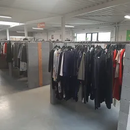 Rekken met tweedehands kleding in verschillende kleuren en stijlen in een grote winkelruimte