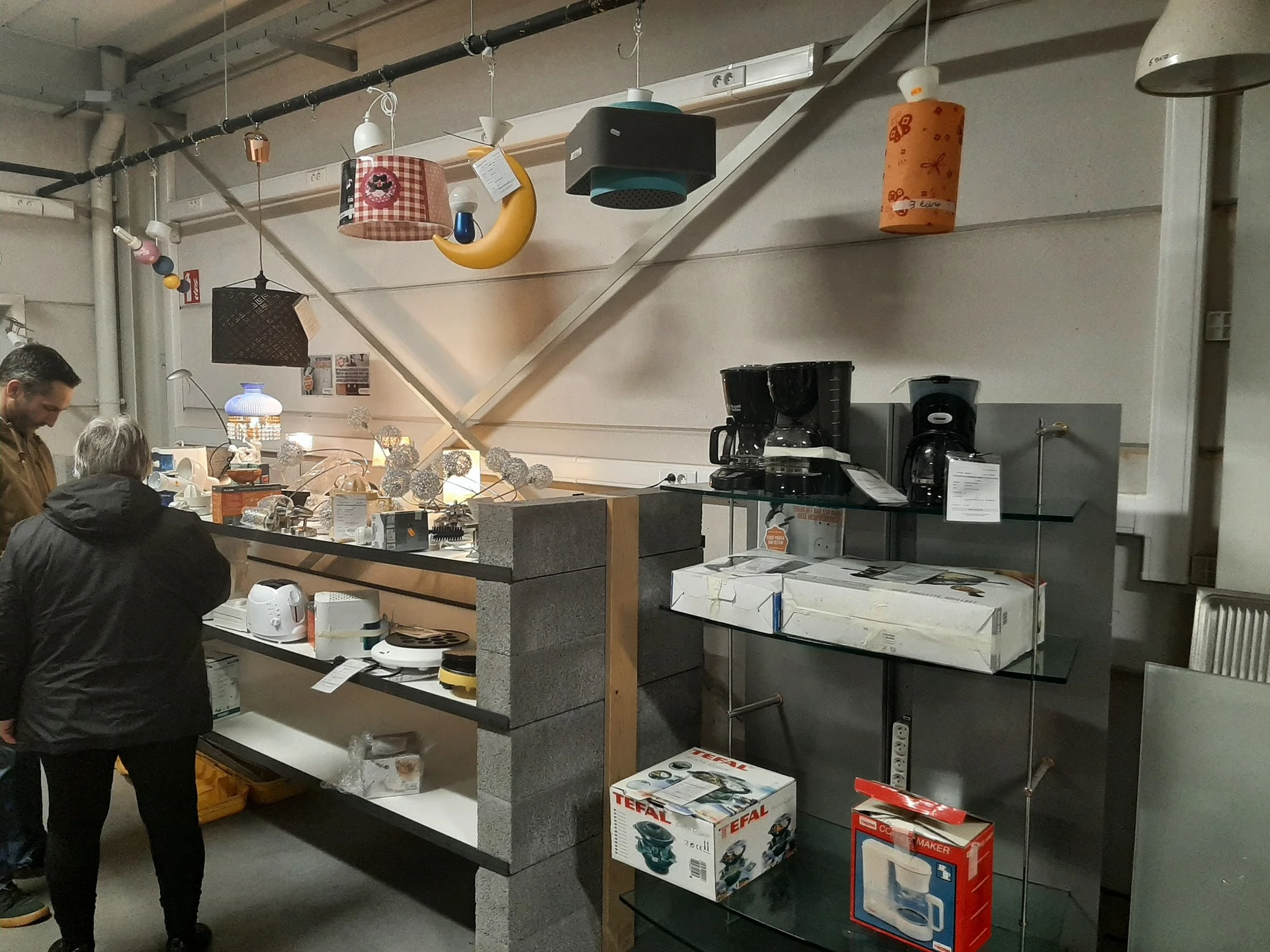 Winkelbinnenkant met toonbank, koffieapparaten en hangdecoratie in een kringloopwinkel