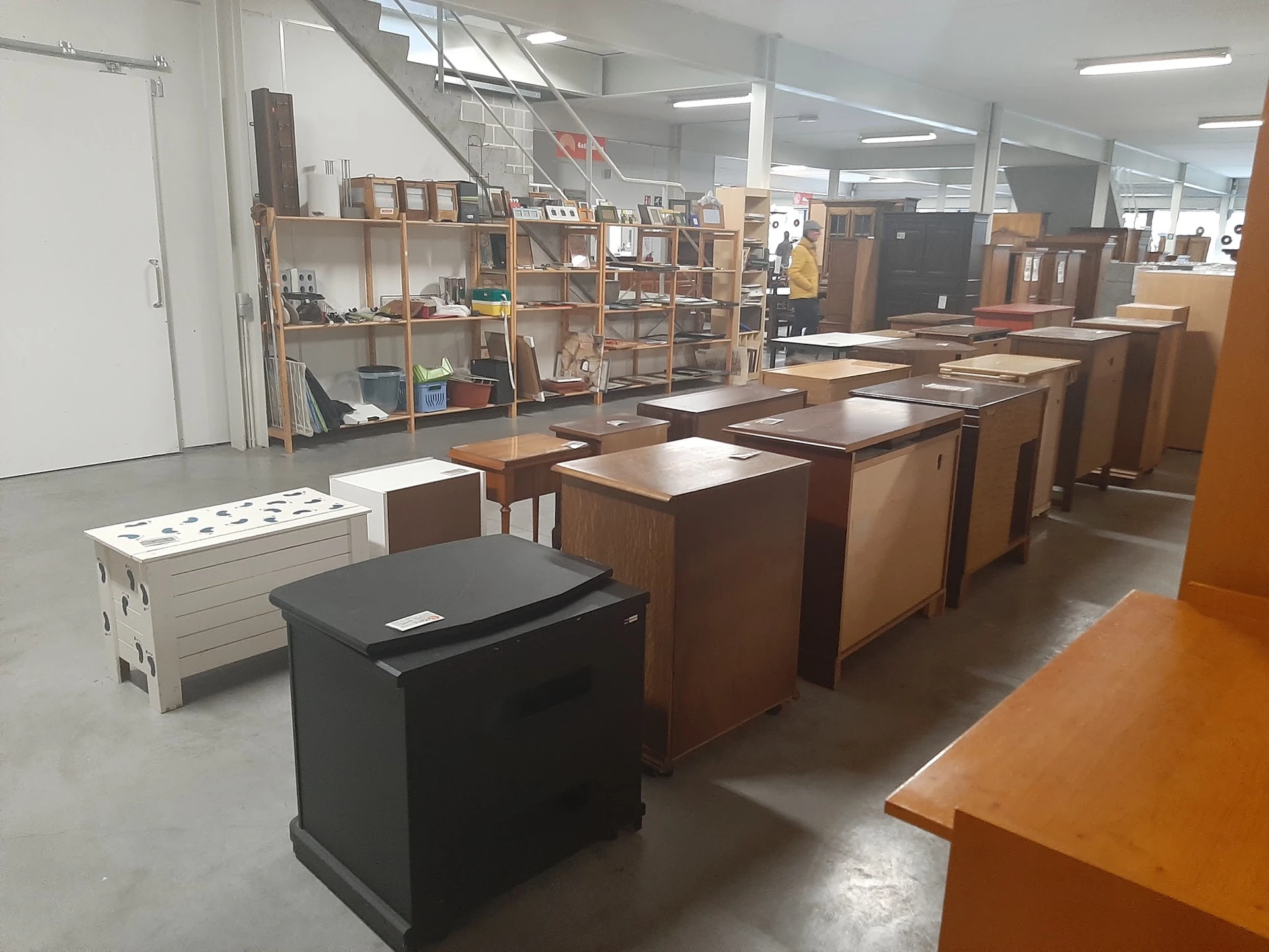 Winkelinterieur met houten meubels, kasten en tafels uitgestald op betonnen vloer onder fluorescerende verlichting