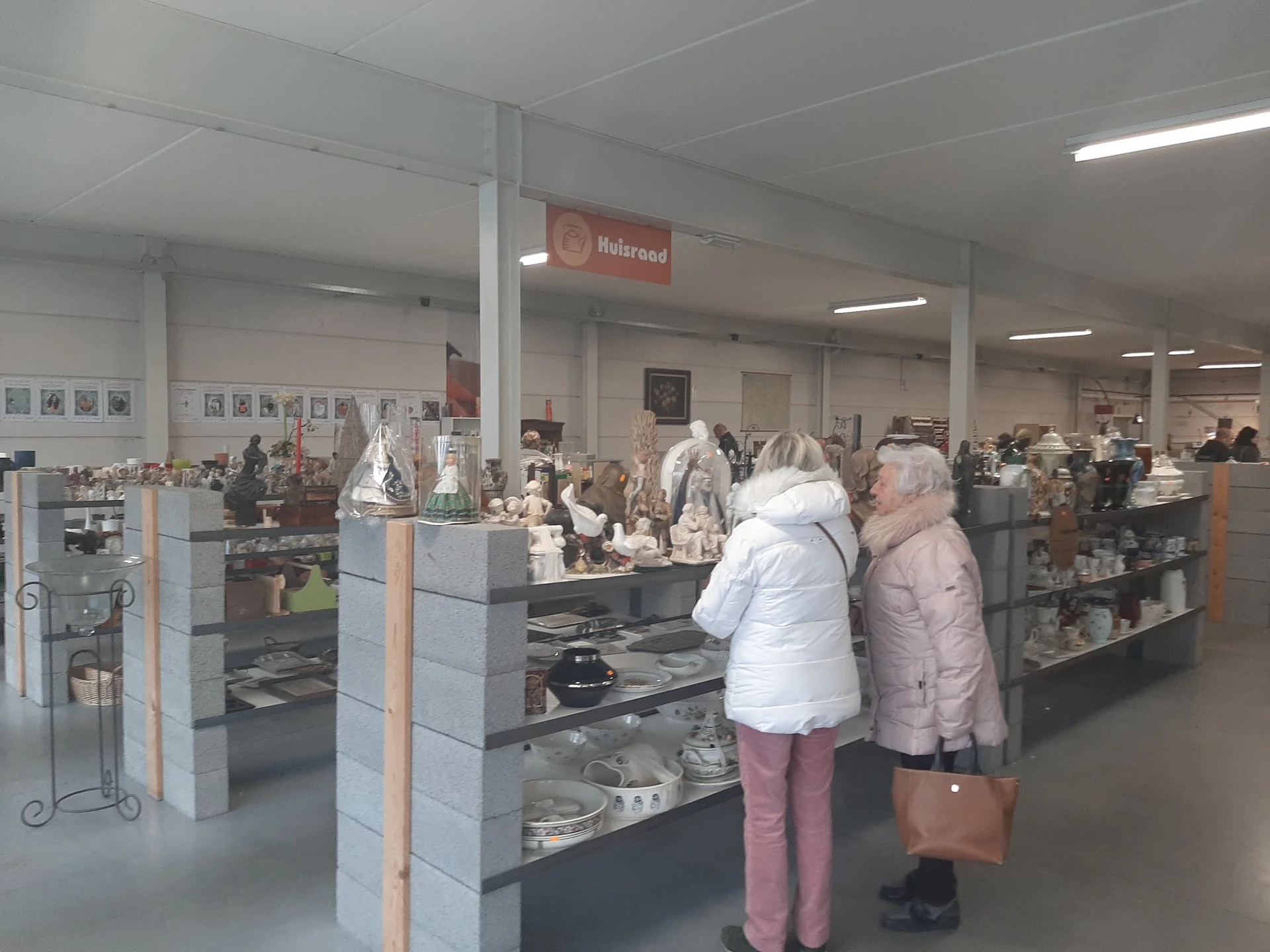Winkelinterieur met vitrines vol aardewerk en decoratieve items, twee klanten bekijken de uitstalling