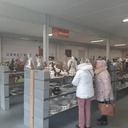 Winkelinterieur met vitrines vol aardewerk en decoratieve items, twee klanten bekijken de uitstalling