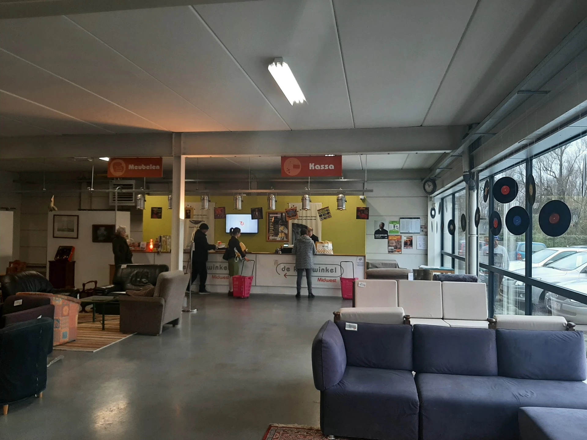 Winkelinterieur met zithoeken, gele infoschermen en balie met medewerkers aan het werk