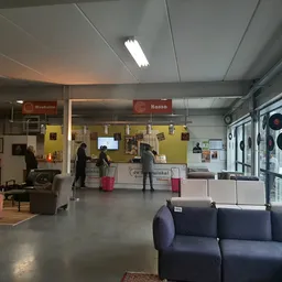 Winkelinterieur met zithoeken, gele infoschermen en balie met medewerkers aan het werk