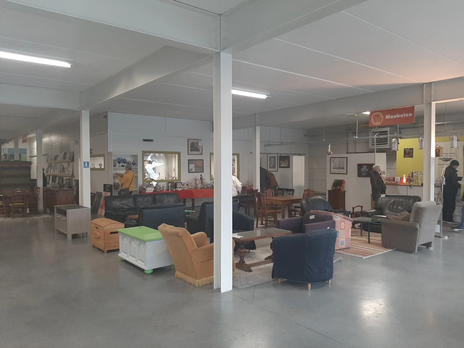 Winkelvloer met verschillende meubelstukken, fauteuils en stoelen verspreid door de ruimte, steunpilaren, plafondverlichting