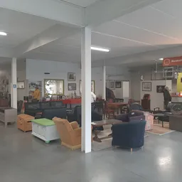 Winkelvloer met verschillende meubelstukken, fauteuils en stoelen verspreid door de ruimte, steunpilaren, plafondverlichting