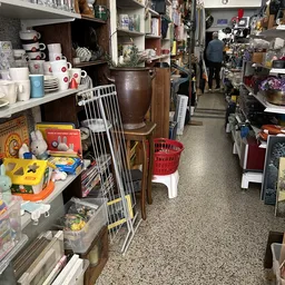 Winkelpad tussen stellingen met huishoudelijk spullen, serviesgoed en diverse gebruiksartikelen in een kringloopwinkel.