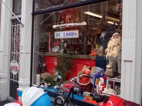 Etalage van kringloopwinkel met DE LOODS-bord, kerststukken, beelden en decoratie achter raam