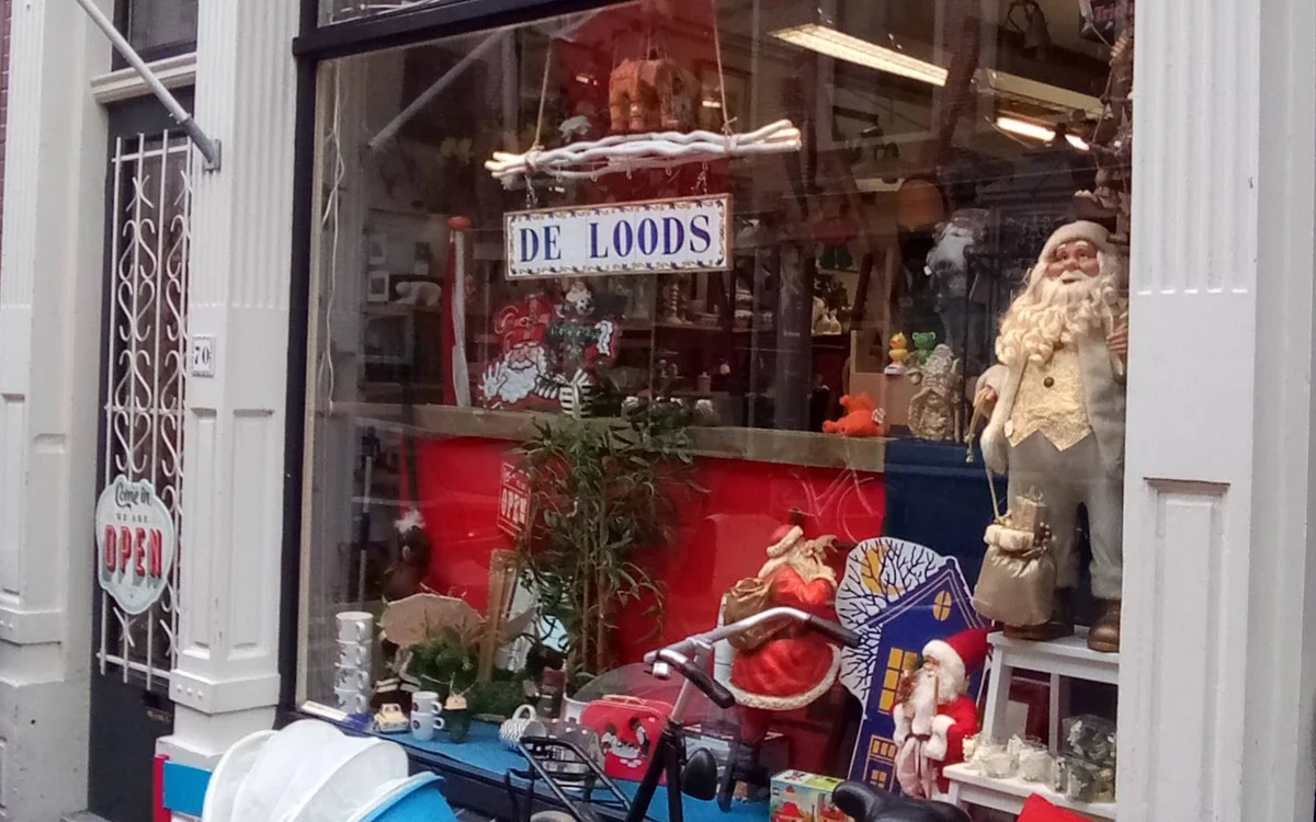 Etalage van kringloopwinkel met DE LOODS-bord, kerststukken, beelden en decoratie achter raam