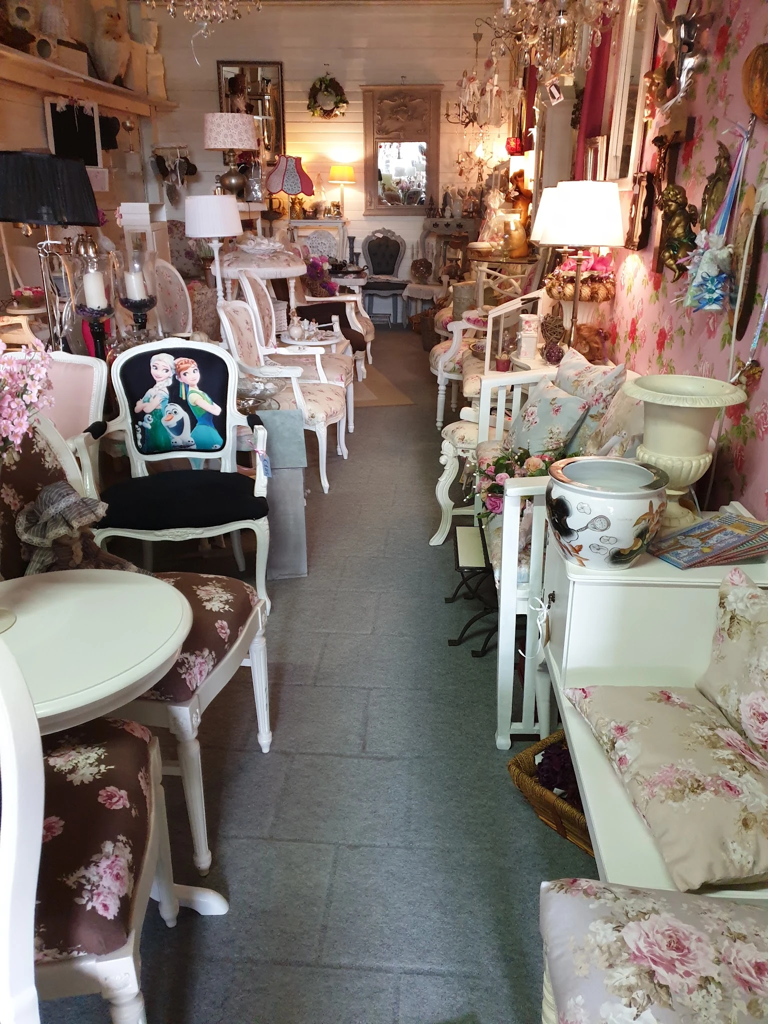 Winkelvloer met witte stoelen en fauteuils met bloemenpatronen, stellingen met decoratieve items in de achtergrond