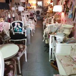 Winkelvloer met witte stoelen en fauteuils met bloemenpatronen, stellingen met decoratieve items in de achtergrond