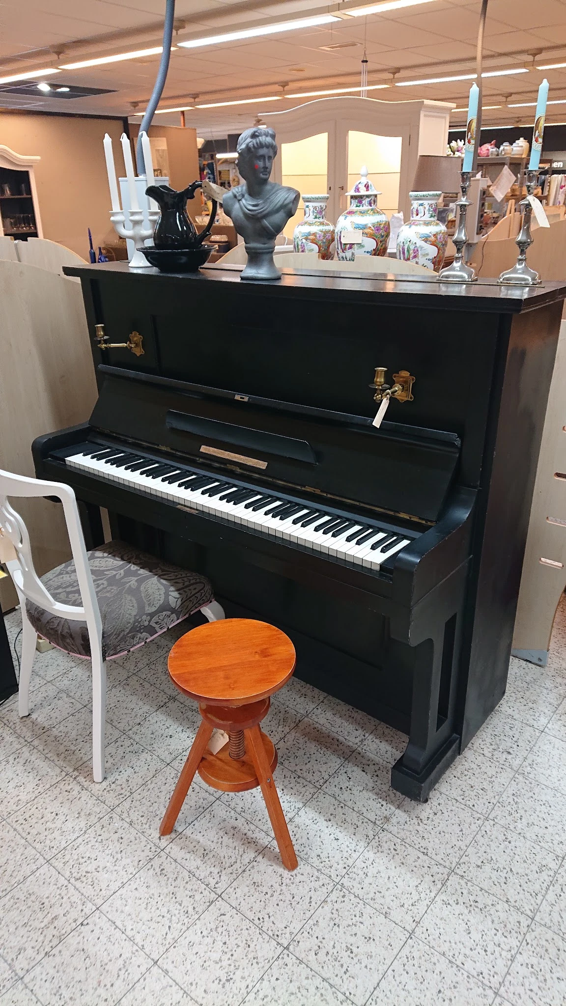Zwarte staande piano met witte toetsen en houten kruk in showroom