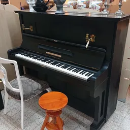 Zwarte staande piano met witte toetsen en houten kruk in showroom