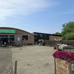 Exterieur van kringloopwinkel De Makelij met groene winkelname op dak, terras met stoelen en bloembakken.