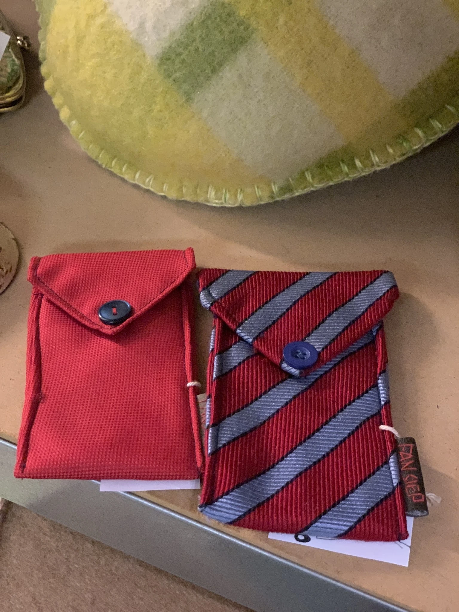 Twee rode portemonnees met blauwe knoopsluiting, één effen en één met blauwe strepenpatroon
