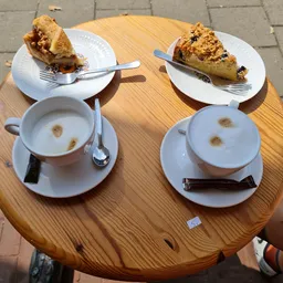 Twee kopjes koffie en twee gebakjes op houten tafel in een lunchroom