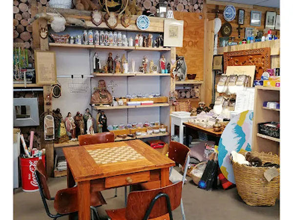 Winkelvloer met houten tafel, stellingen vol decoratieve items, servies en kunstvoorwerpen tegen de muren
