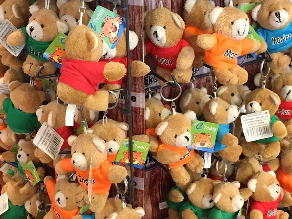 Verzameling knuffelberen met kleurrijke kleding en labels, opgehangen in een winkelrek