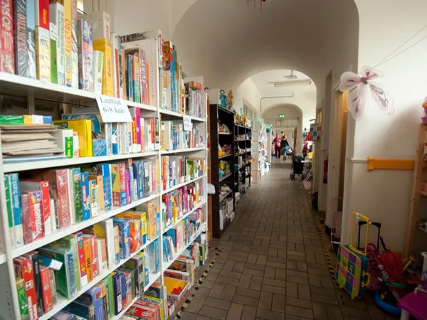 Lange gang met boekenrekken vol tweedehands boeken aan de linkerkant, posters aan de rechtermuur