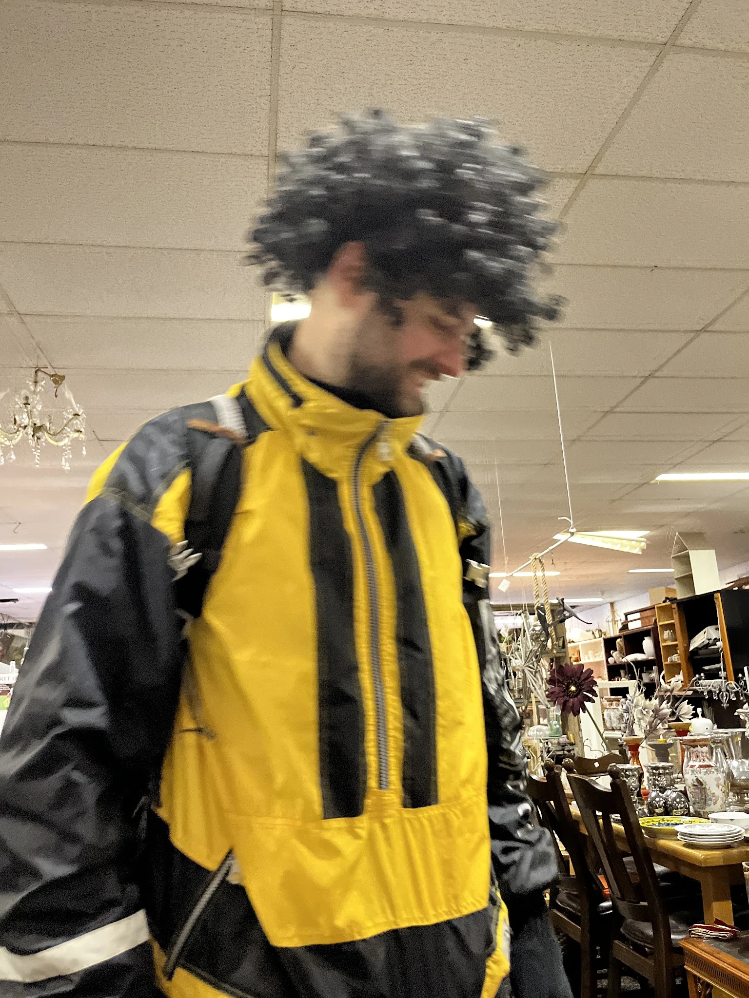 Persoon in geel-zwart jack in de winkel tussen stellingen met spullen