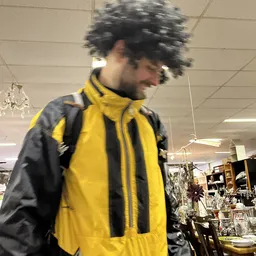 Persoon in geel-zwart jack in de winkel tussen stellingen met spullen