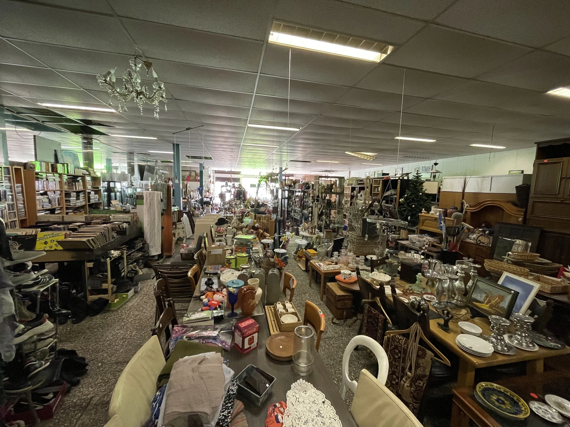 Overzicht van de winkelvloer met diverse kringloopwaar: meubels, servies, decoratie en huishoudartikelen op tafels en stellin
