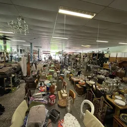Overzicht van de winkelvloer met diverse kringloopwaar: meubels, servies, decoratie en huishoudartikelen op tafels en stellin