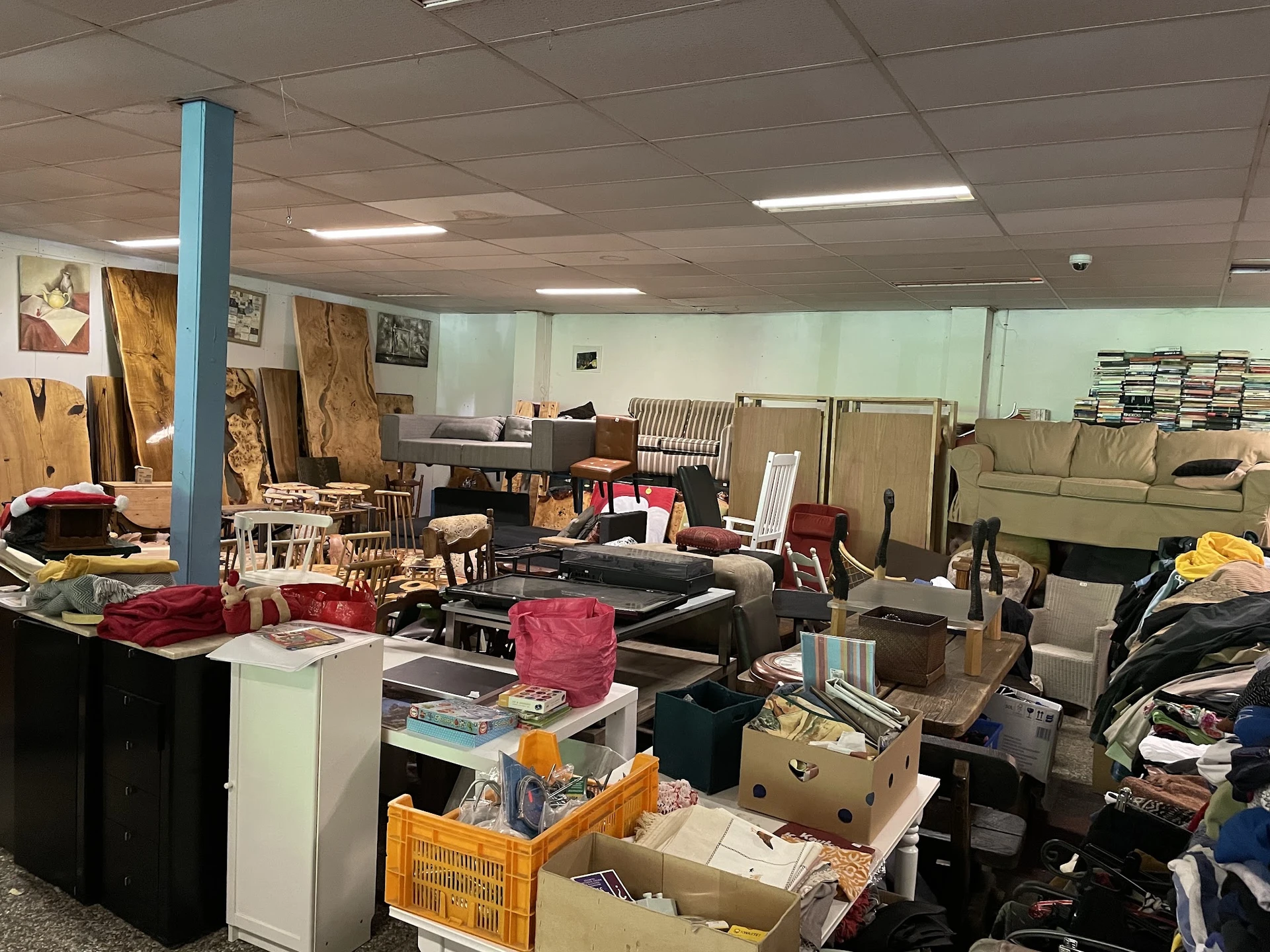 Rommelig winkelinterieur met meubels, dozen, kleding en huishoudelijke artikelen verspreid op de vloer en planken