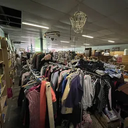 Rekken met tweedehands kleding in verschillende kleuren in een kringloopwinkel
