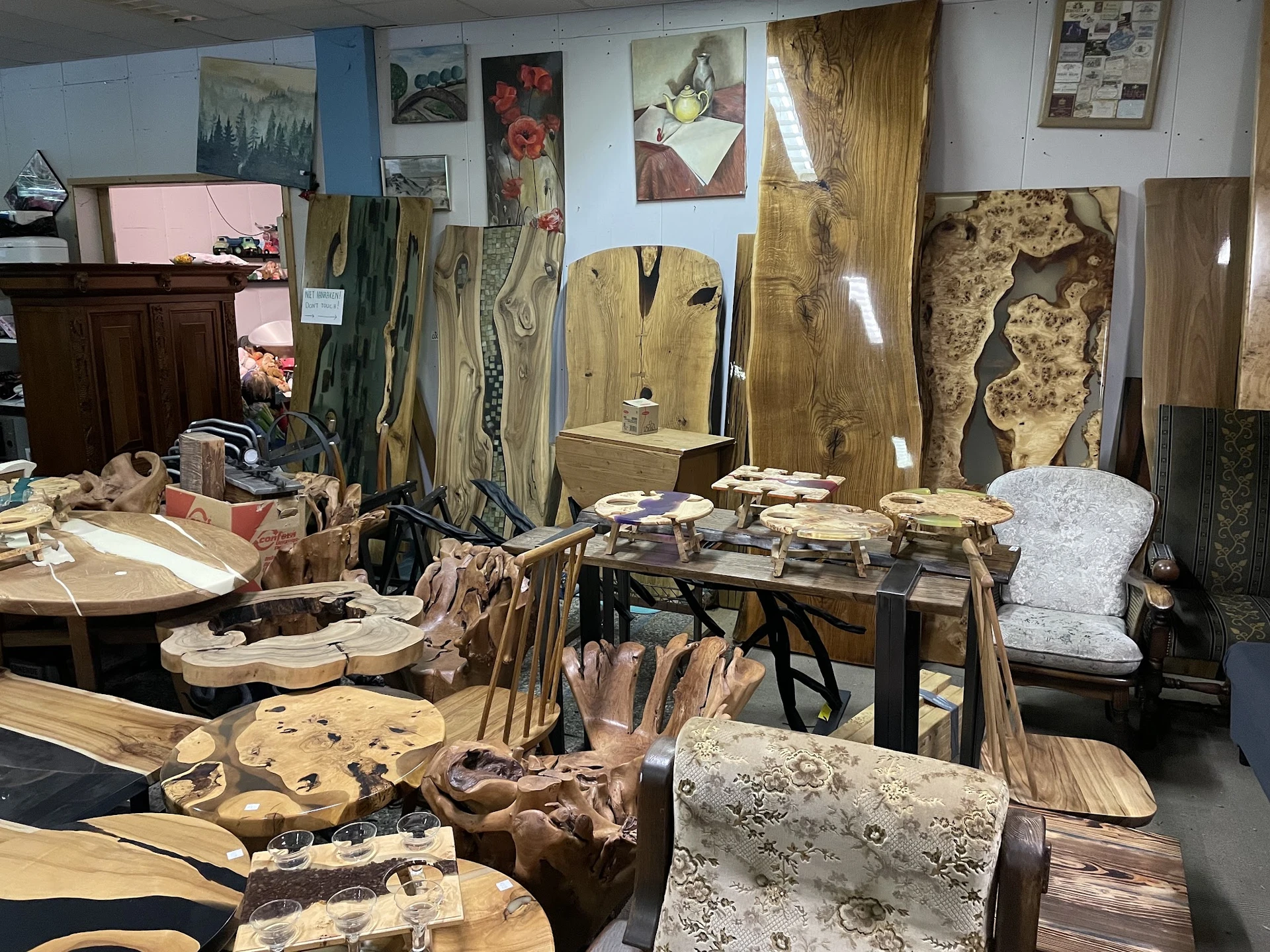Uitgestalde houten meubels en decoratieve objecten in de kringloopwinkel, waaronder houten panelen, sculpturen en handwerk.