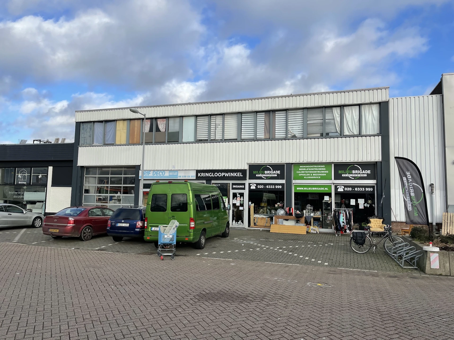 Gevel van kringloopwinkel met groene bus en parkeerplaats aan straatkant
