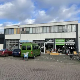 Gevel van kringloopwinkel met groene bus en parkeerplaats aan straatkant