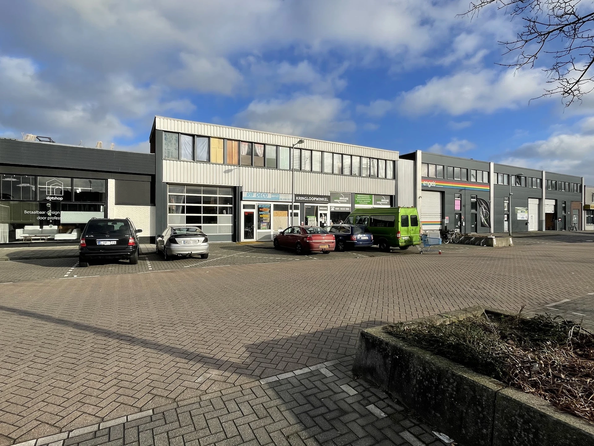 Grijswit industrieel pand met meerdere units aan parkeerplaats met enkele auto's
