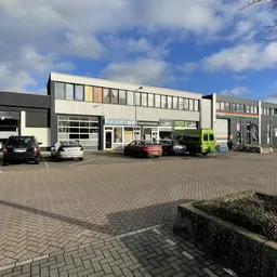 Grijswit industrieel pand met meerdere units aan parkeerplaats met enkele auto's