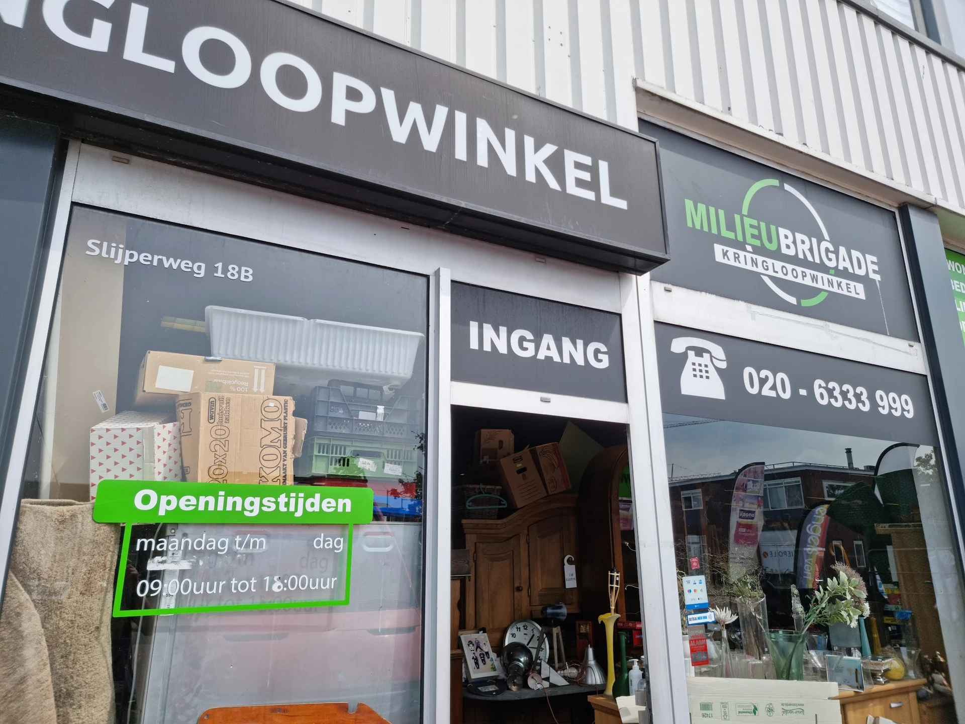 Gevel van Milieu Brigade Kringloopwinkel met uithangbord, winkelraam en ingang aan Slijperweg