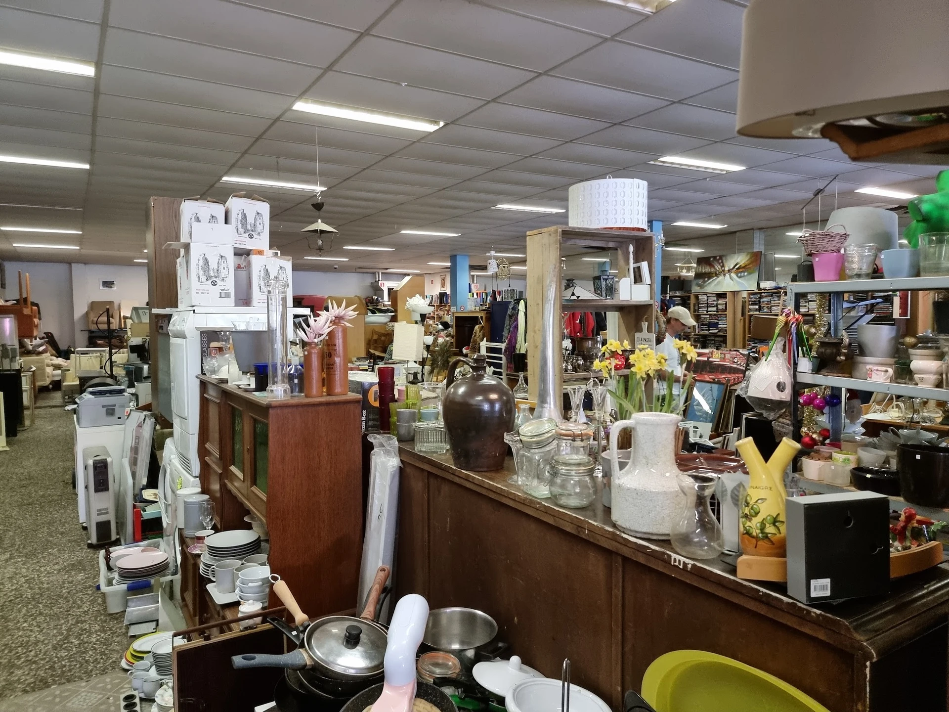 Overzicht van de winkelvloer met toonbanken, stellingen vol huishoudartikelen, servies, decoratie en diverse tweedehands spul