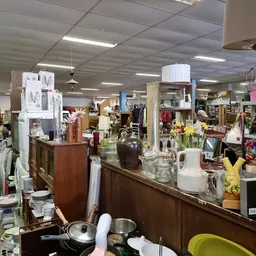 Overzicht van de winkelvloer met toonbanken, stellingen vol huishoudartikelen, servies, decoratie en diverse tweedehands spul