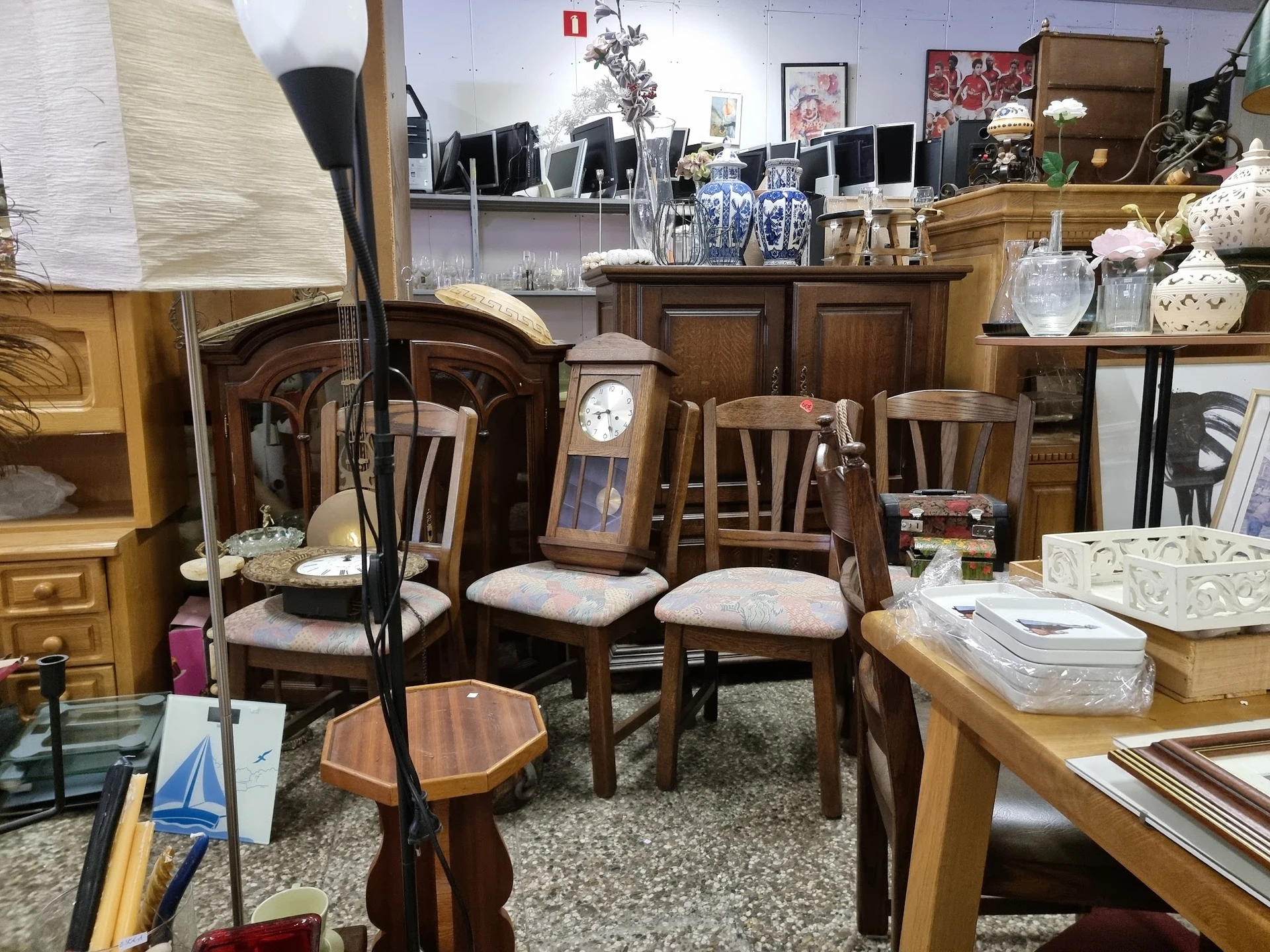 Houten meubels en huishoudelijke artikelen uitgestald in een kringloopwinkel, met stoelen, tafels, lampen en decoratieve item