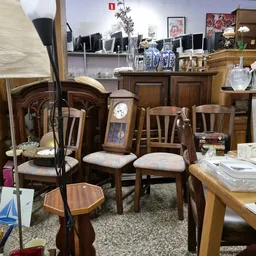 Houten meubels en huishoudelijke artikelen uitgestald in een kringloopwinkel, met stoelen, tafels, lampen en decoratieve item