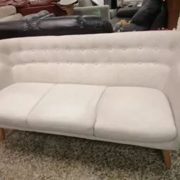 Witte gestoffeerde bank met knoopstiksels en houten poten, op karpet in winkel