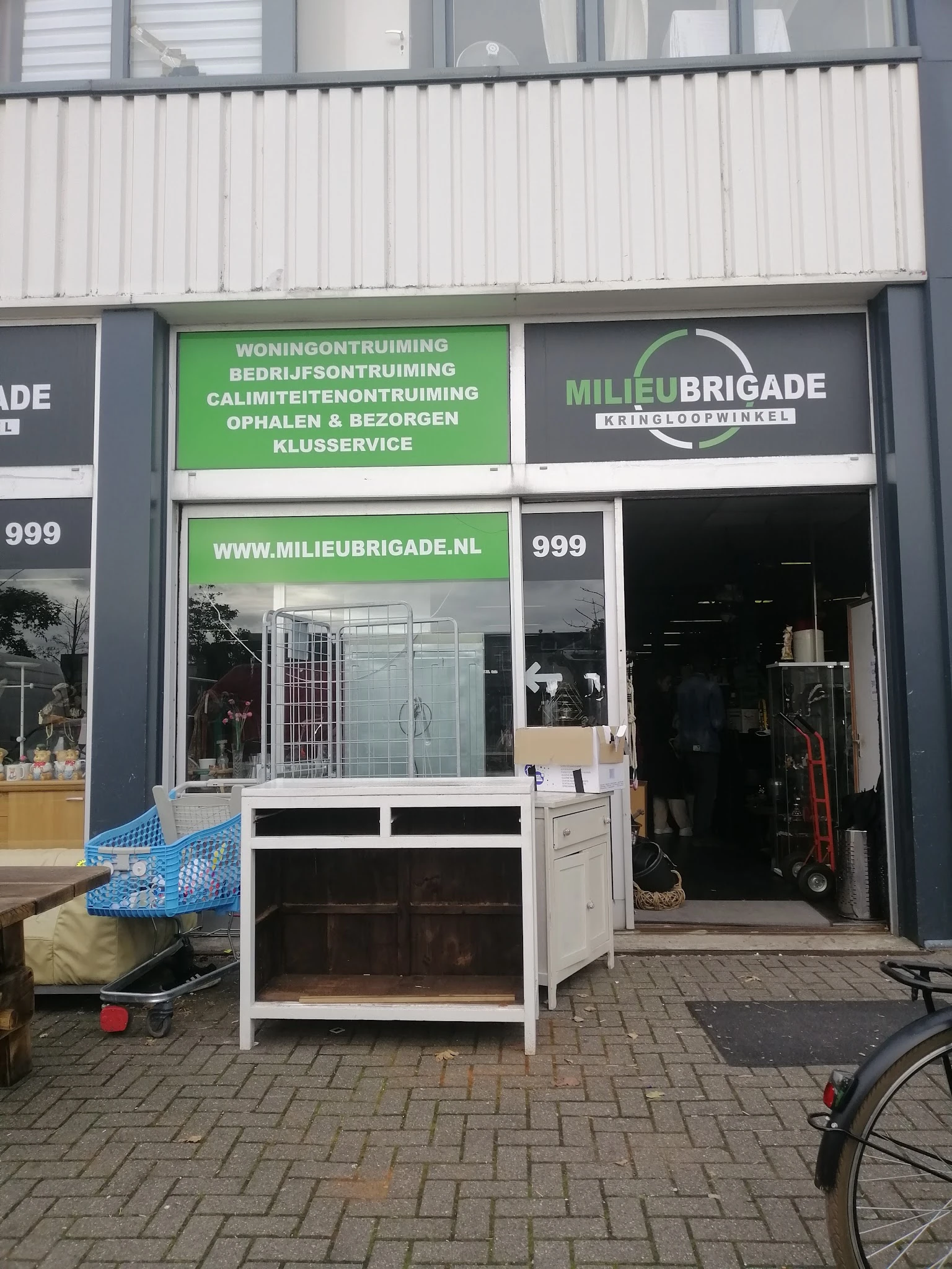 Winkelgevel met groene en zwarte belettering, vitrine met dameskleding, ingang met witte deur