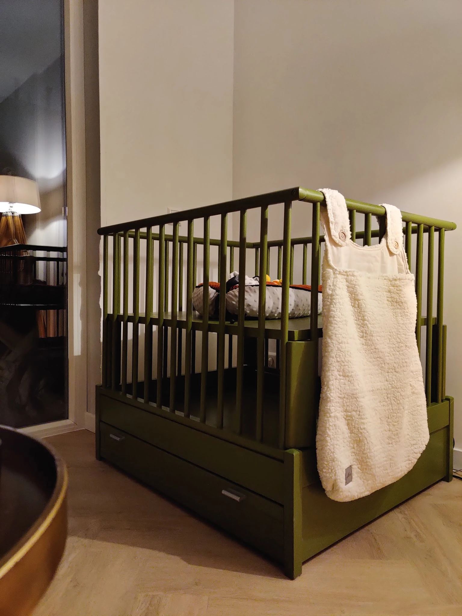Tweedehands babybed met zwart frame en groen-gele details, inclusief witte beddensprei