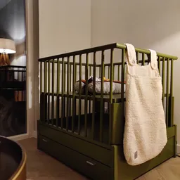 Tweedehands babybed met zwart frame en groen-gele details, inclusief witte beddensprei