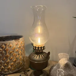 Antieke olielamp met glazen kap en decoratieve metalen voet, verlicht weergegeven