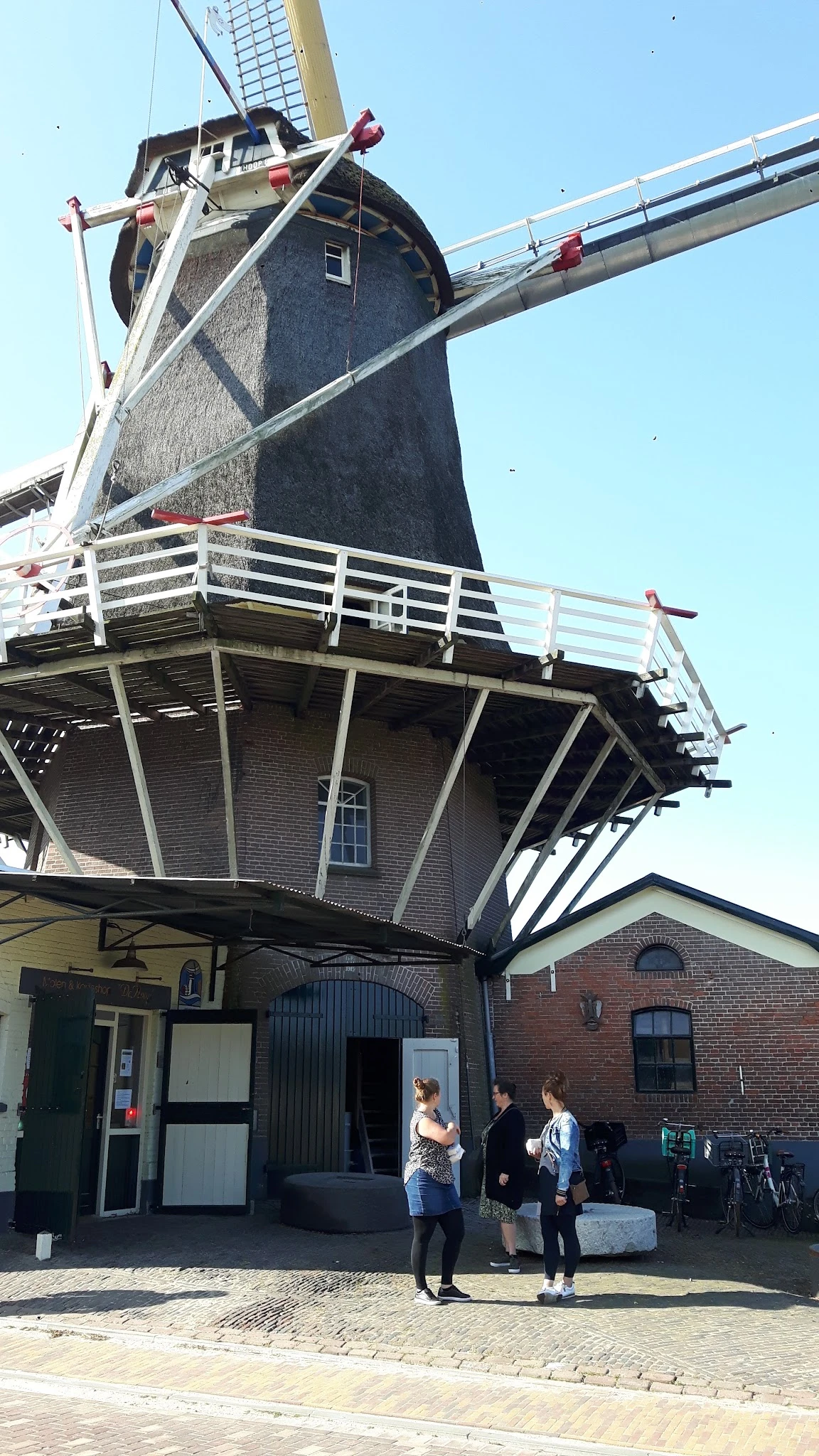 Bakhuismolen met bakstenen onderbouw en houten draaidak, witte reling zichtbaar, onderdeel van kringloopwinkel De Olde Bakker